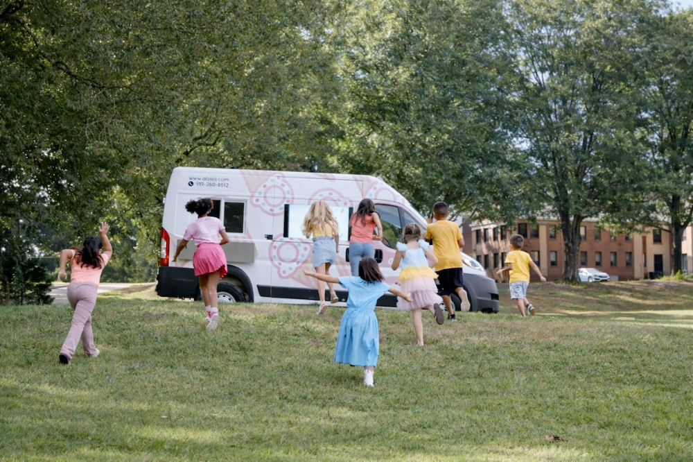 Kids running through green grass on a summer day towards an ice cream truck.