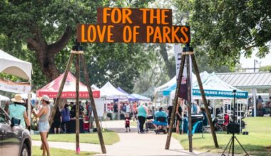 This image depicts a wooden event sign that reads, "For the Love of Parks," at Richard Moya Park. There are several tents in the background featuring different businesses and organizations.