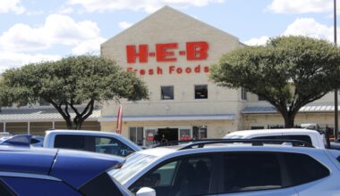 Exterior of white Buda H-E-B location with red letterring and two trees.