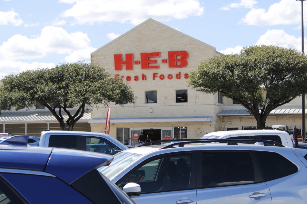 Exterior of white Buda H-E-B location with red letterring and two trees.