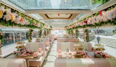 The upstairs floor of a double-decker bus decorated with pink flowers and decorations.