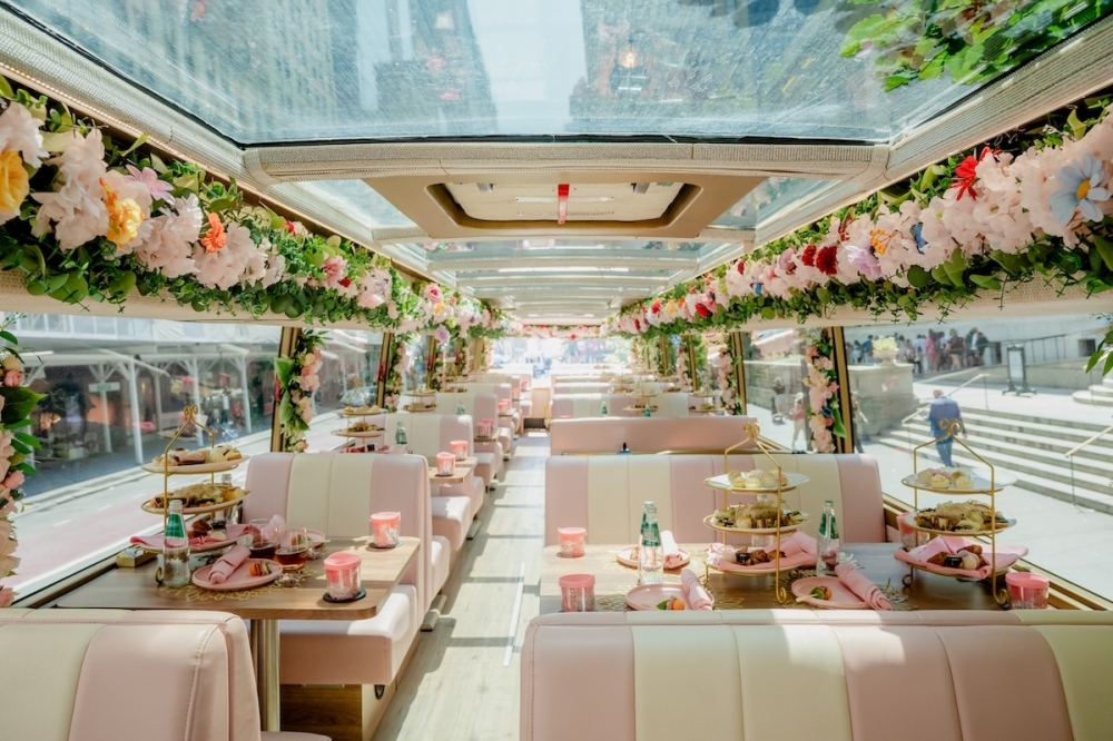 The upstairs floor of a double-decker bus decorated with pink flowers and decorations.