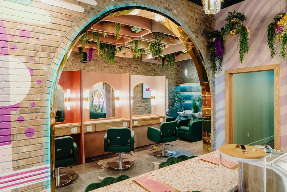 A beauty salon with a colorful brick arch and green seats in front of lit mirrors