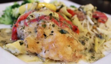 Lightly breaded meat on a bed of pasta topped with vegetables and sauce on a white plate.