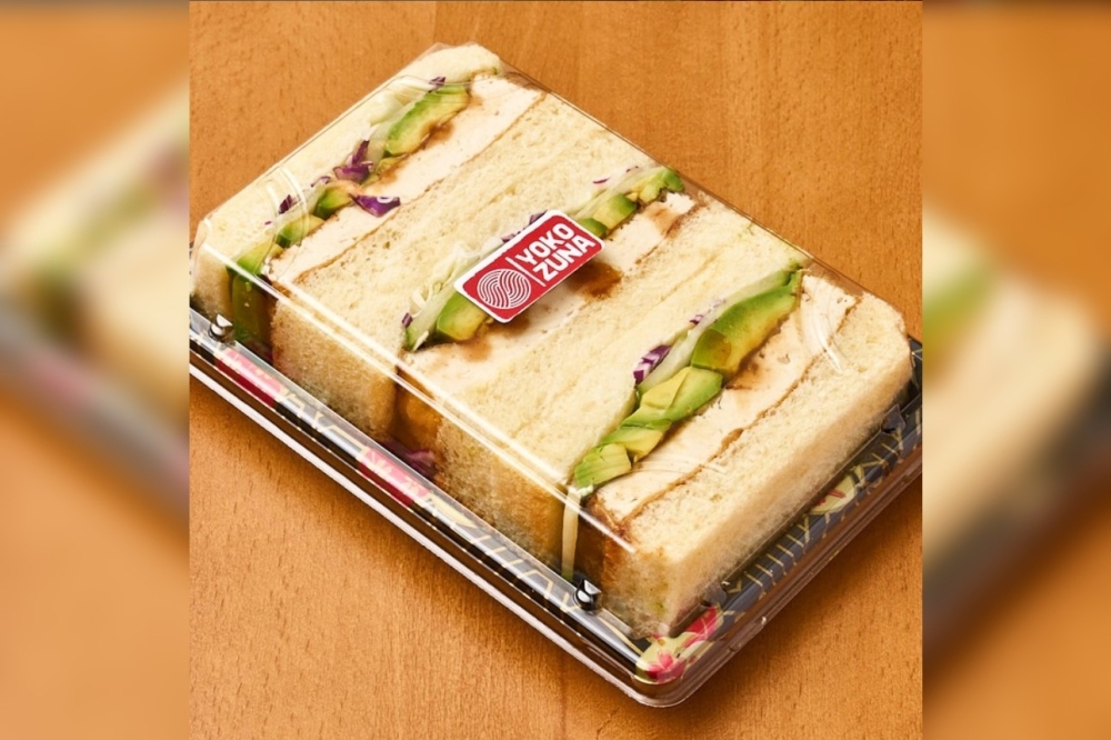 A sandwich cut into three equal part and packaged in a to-go container with a clear lid