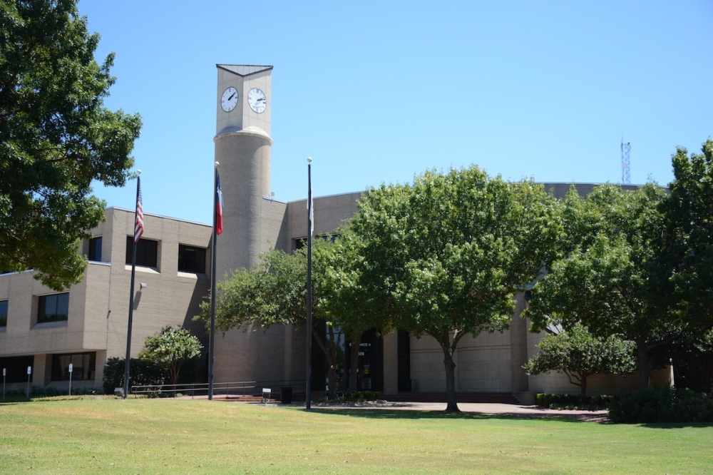 The exterior of the Plano Municipal Center, a blocky gray building, partially obscured by trees