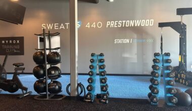 Interior of a gym featuring a variety of dumbbells on racks and Sweat440 Prestonwood signage.