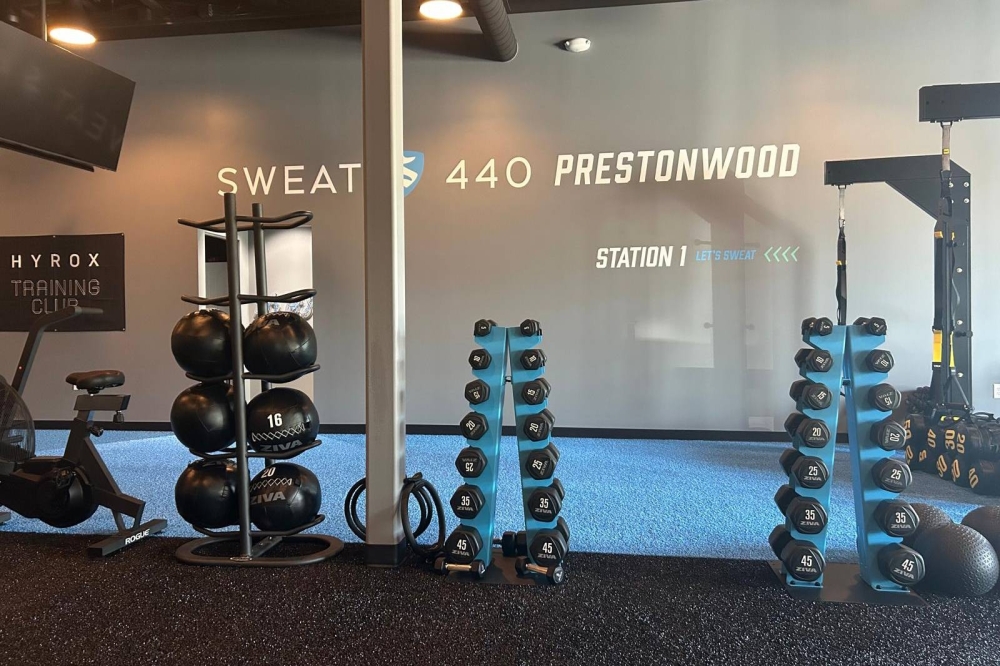 Interior of a gym featuring a variety of dumbbells on racks and Sweat440 Prestonwood signage.