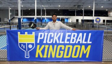 Male standing behind a Pickleball Kingdom banner in an indoor pickleball business.