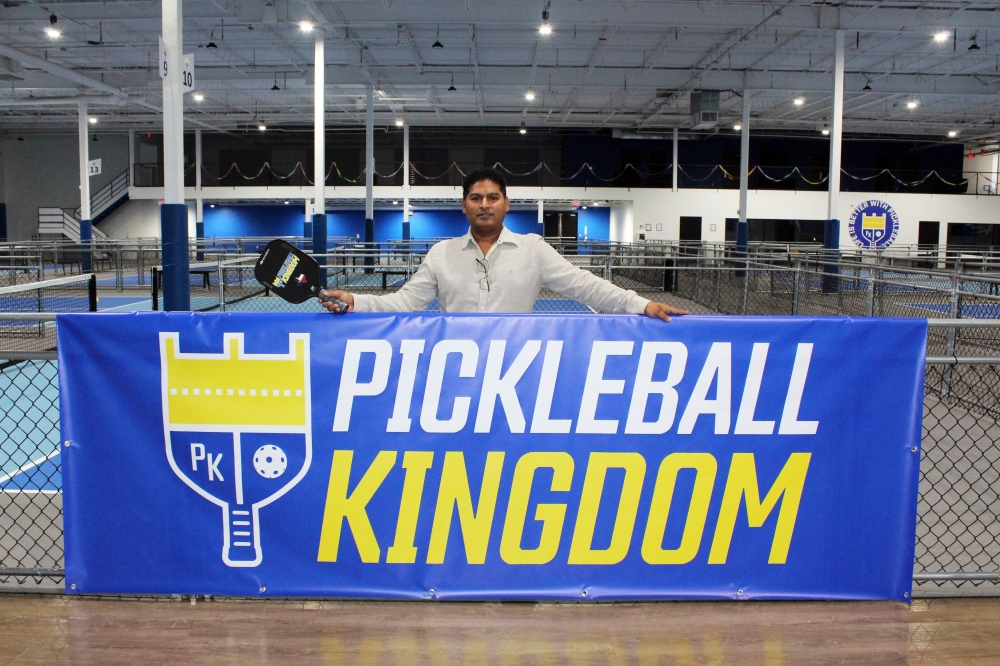 Male standing behind a Pickleball Kingdom banner in an indoor pickleball business.