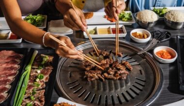 Overview of people's hands cooking strips of meat on a table-top grill.