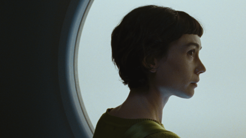 Actress Sydney Chandler looks to her right in front of a window in a still image from the film 