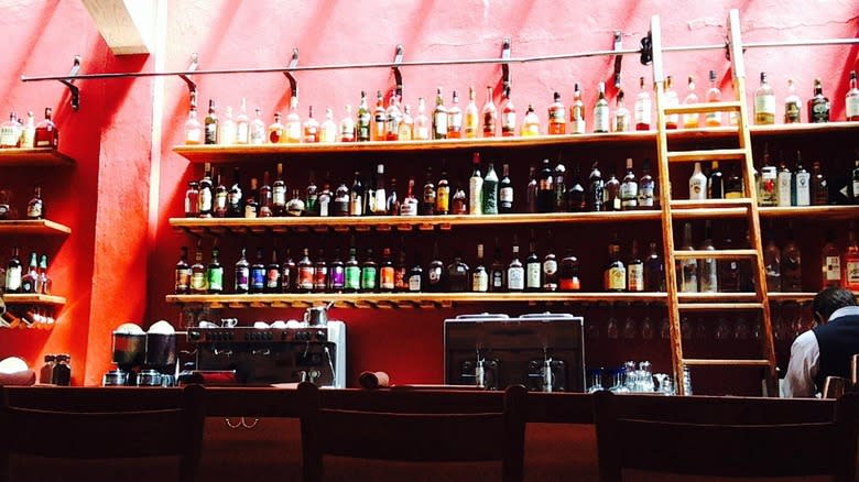 Bottles of liquor line bright colored wall behind bar