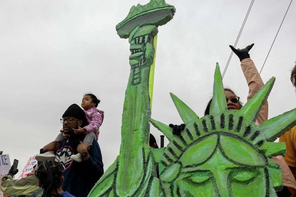 Protesters stand beside a styrofoam Statue of Liberty as traffic passes by during a No Kings protest March 28, 2026 in Frisco. (Azul Sordo/Staff Photographer)