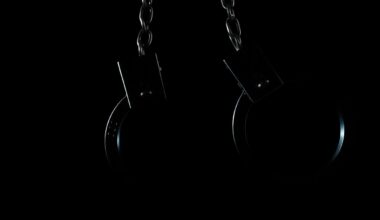 An extreme close-up photograph of a pair of metal handcuffs against a stark black background, conceptually representing the consequences of a serious crime.