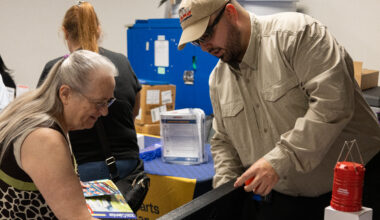 an elderly woman talks to a man wearing a ballcap and glasses at a public event for emergency preparedness.