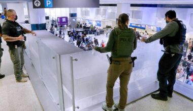 Federal immigration agents peer over railings on the floor above the lines of air travelers progressing to the TSA security checkpoint in Terminal C at the George Bush Intercontinental Airport, Monday, March 23, 2026, in Houston. (AP Photo/Michael Wyke)