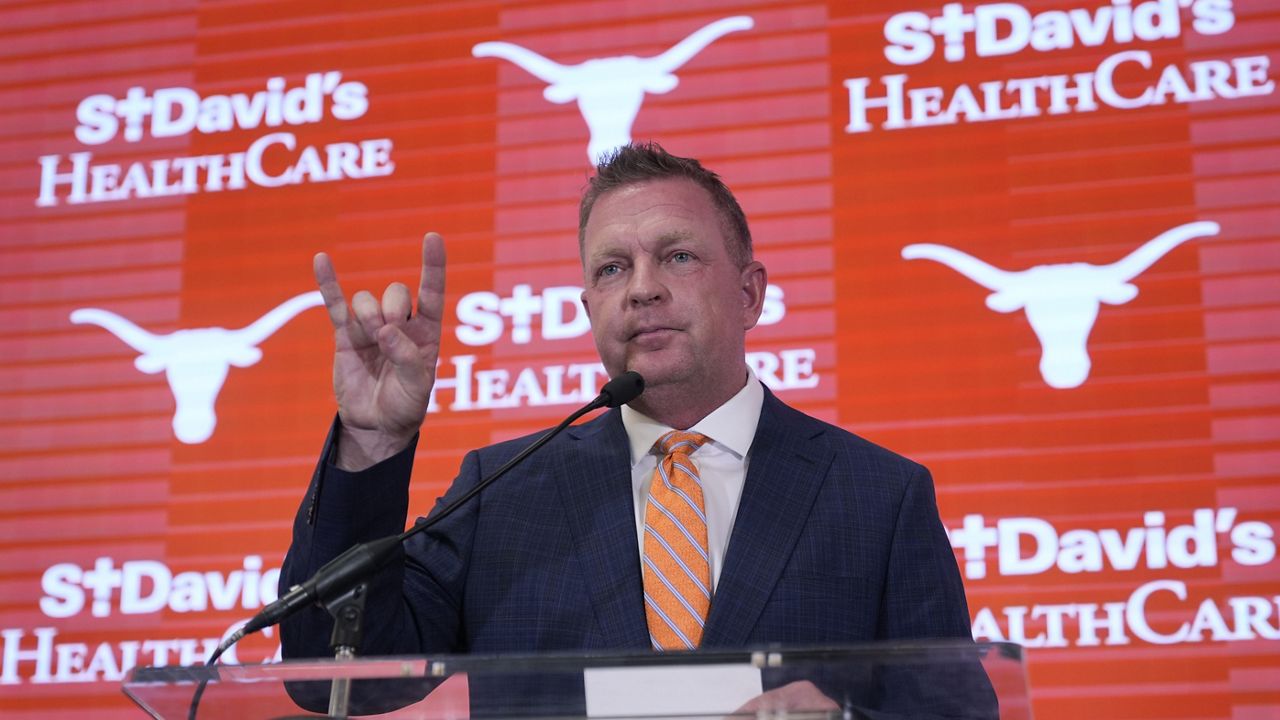 Jim Schlossnagle flashes a hook'em sign as he speaks at a news conference after he was introduced as the new NCAA college head baseball coach at Texas, Wednesday, June 26, 2024, in Austin, Texas. Schlossnagle left rival program Texas A&M. (AP Photo/Eric Gay)