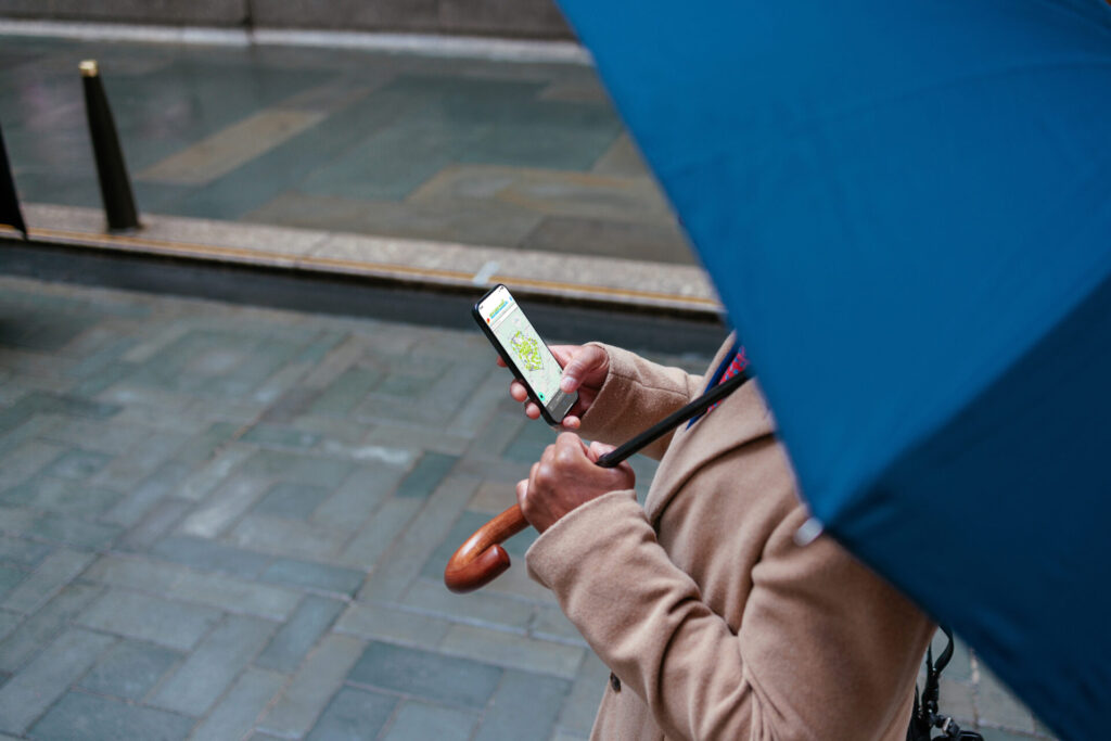 A person holds a cellphone in one hand and an umbrella in another