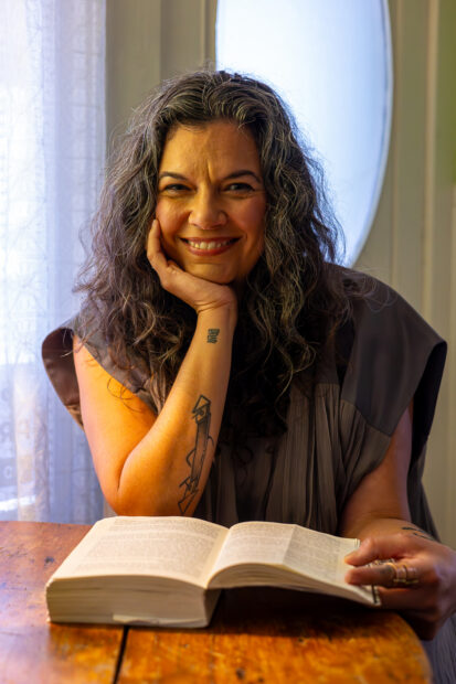 A photograph of curator and writer Leslie Moody Castro with an open book at a wooden table.