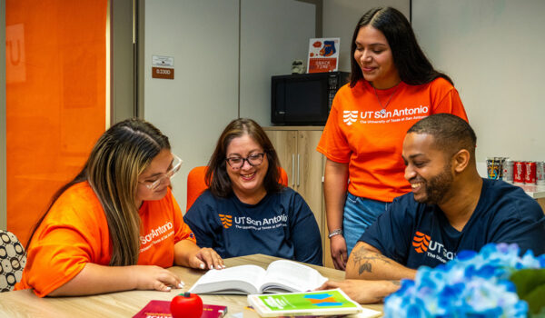 Four people in UT San Antonio t-shirts smile during a conversation at the COEHD Student Success Center