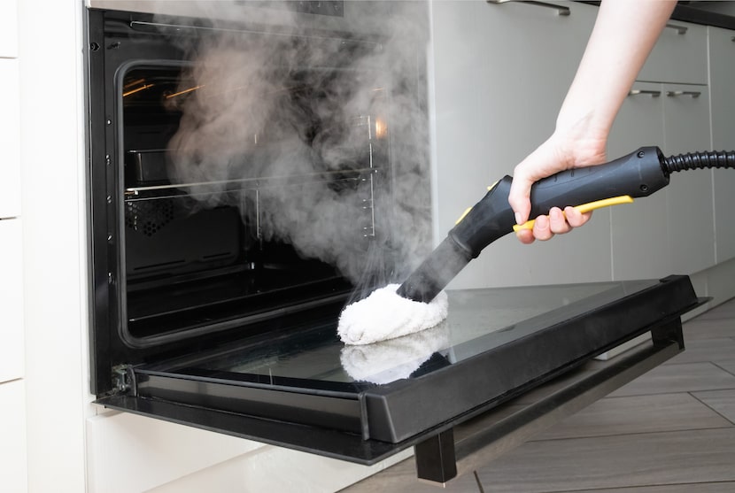Kitchen cleaning. Close up of steam cleaner nozzle sanitizing oven door with visible vapor...