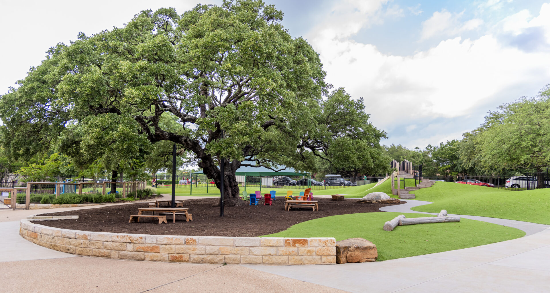 a large oak tree with picnic tables and a playscape