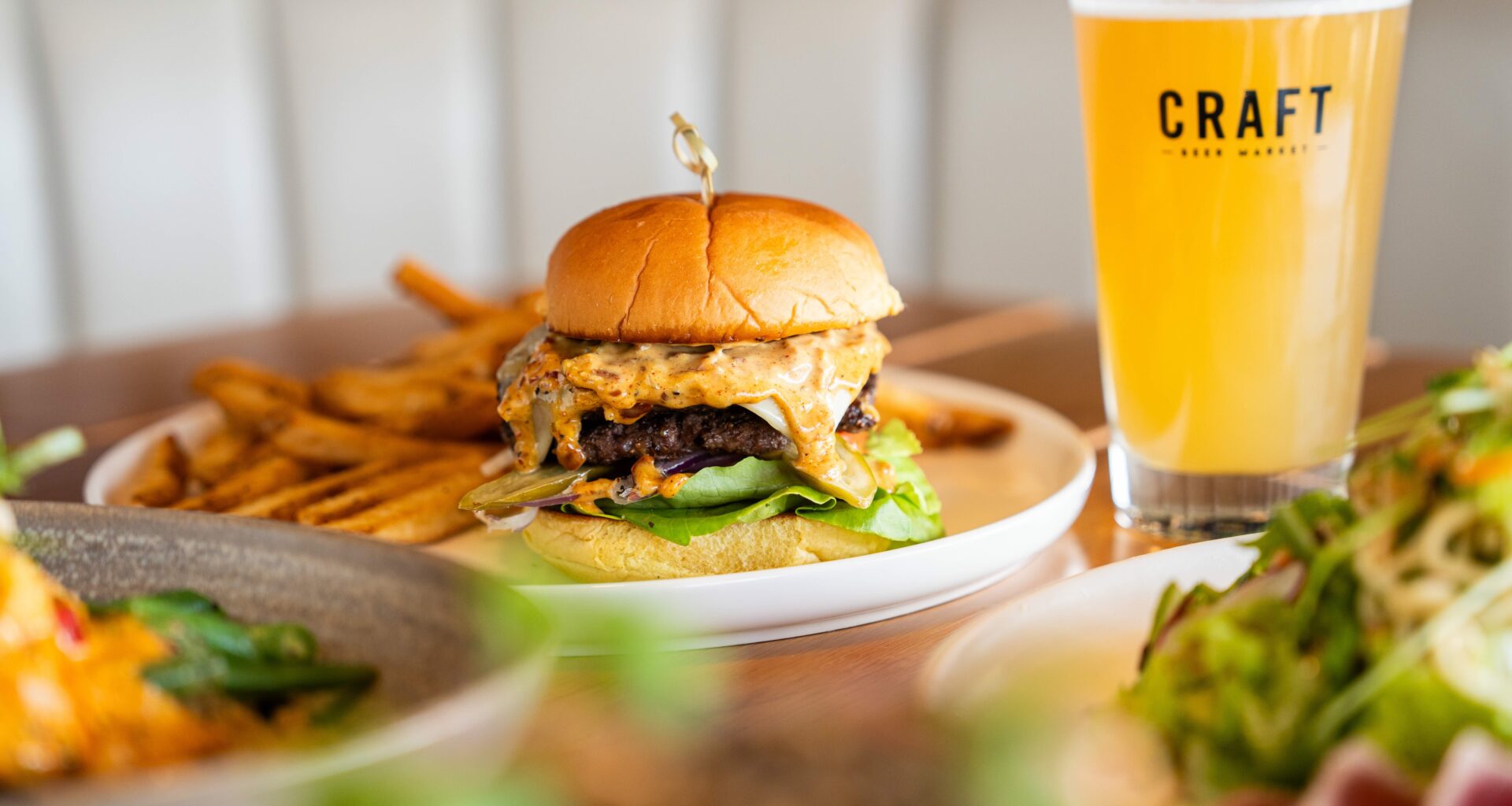 A large burger oozing with cheese and a beer.