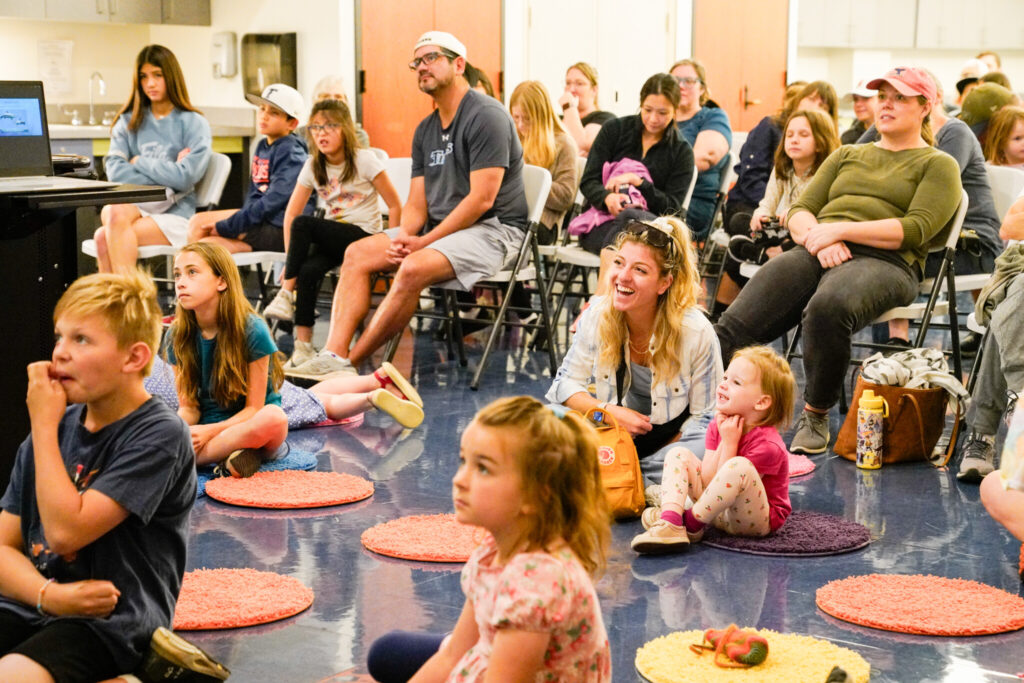 children sitting on carpet circles and parents sitting in chairs behind them, listening to a storytime at the Bullock.