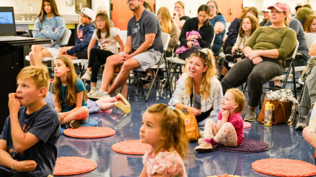 children sitting on carpet circles and parents sitting in chairs behind them, listening to a storytime at the Bullock.