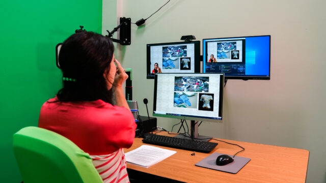A woman sitting in front of three computer screens teaching a virtual class.