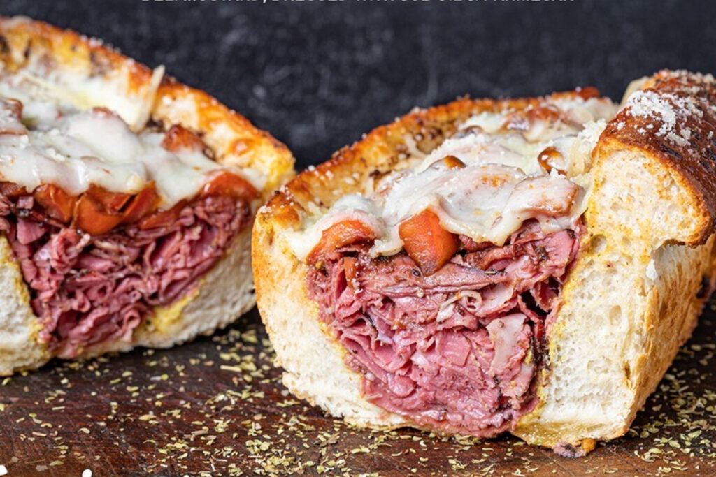 Image shows The Deniro sandwich at Tony's Italian Delicatessen in Texas featuring pastrami under melted Provolone cheese on a crusty Italian roll.