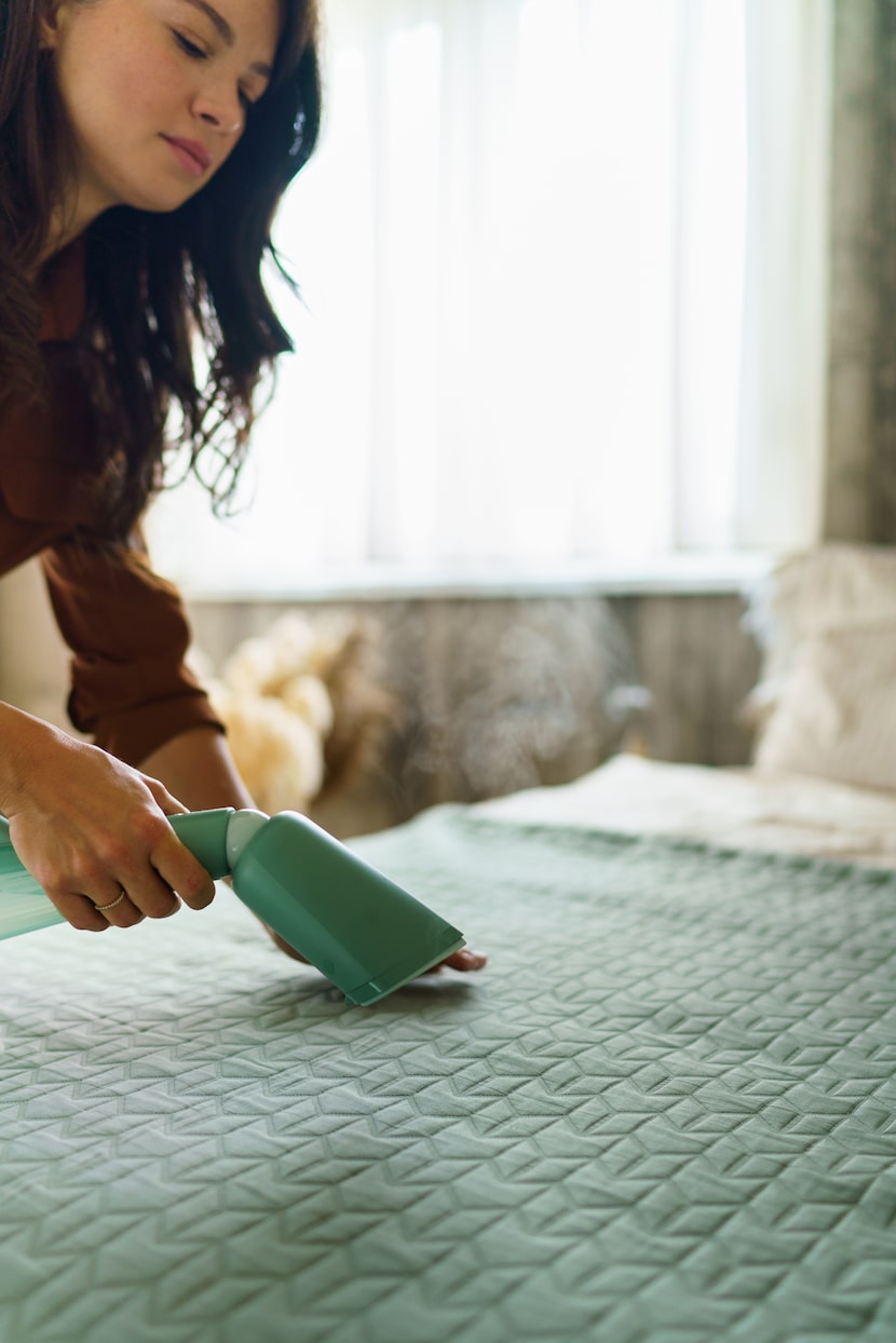 Woman cleaning textile bed mattress using a steam cleaner for hygiene and sanitation.