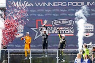 IndyCar driver Kyle Kirkwood (center) raises the winners trophy alongside second place...