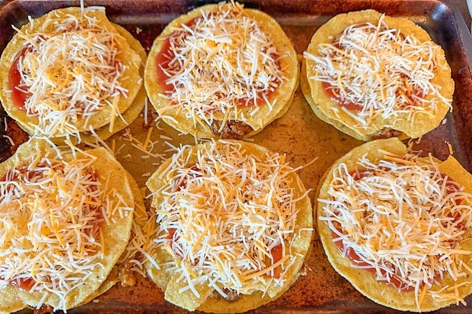 Mexican Pizzas are being prepared in a baking tray, ready to go in oven for baking