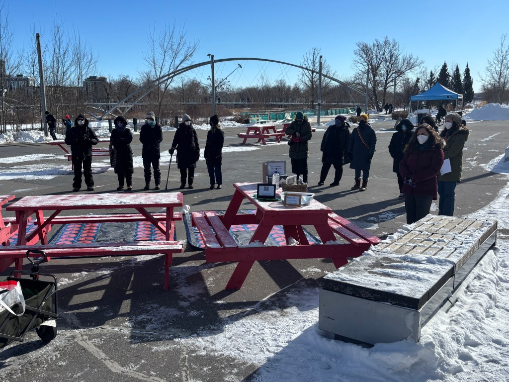 Members of the Canadian Covid Society in Calgary gather outdoors in front of picnic tables and their art display for Long COVID Awareness Day.