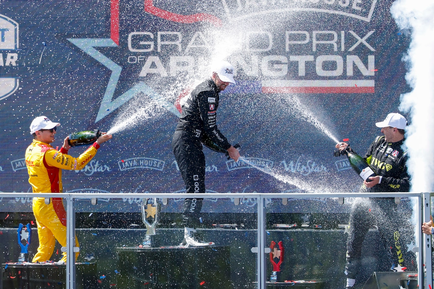 Race winner Kyle Kirkwood sprays champagne on the podium with runner-up Alex Palou and third...