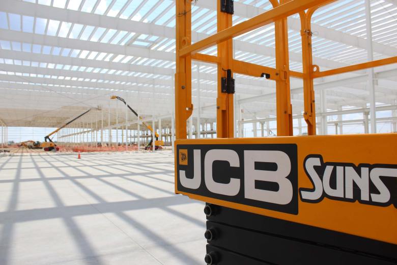 JCB's manufacturing plant under construction near Palo Alto Road on Oct. 16, 2025. A series of steel girders painted white and held up by similar columnns with yellow JCB construction vehicles around the large, concrete floor.
