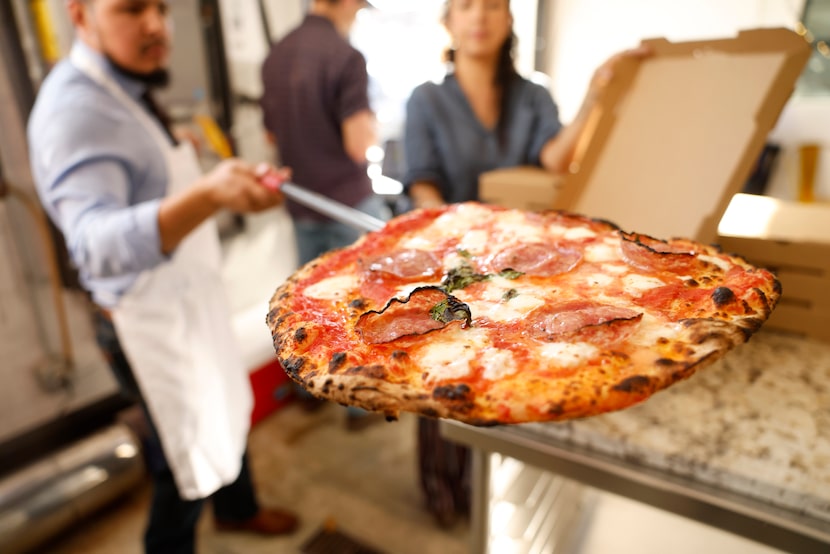 A fired pizza made with pomodoro, hot soppressata, hot honey and ricotta is pulled from the...
