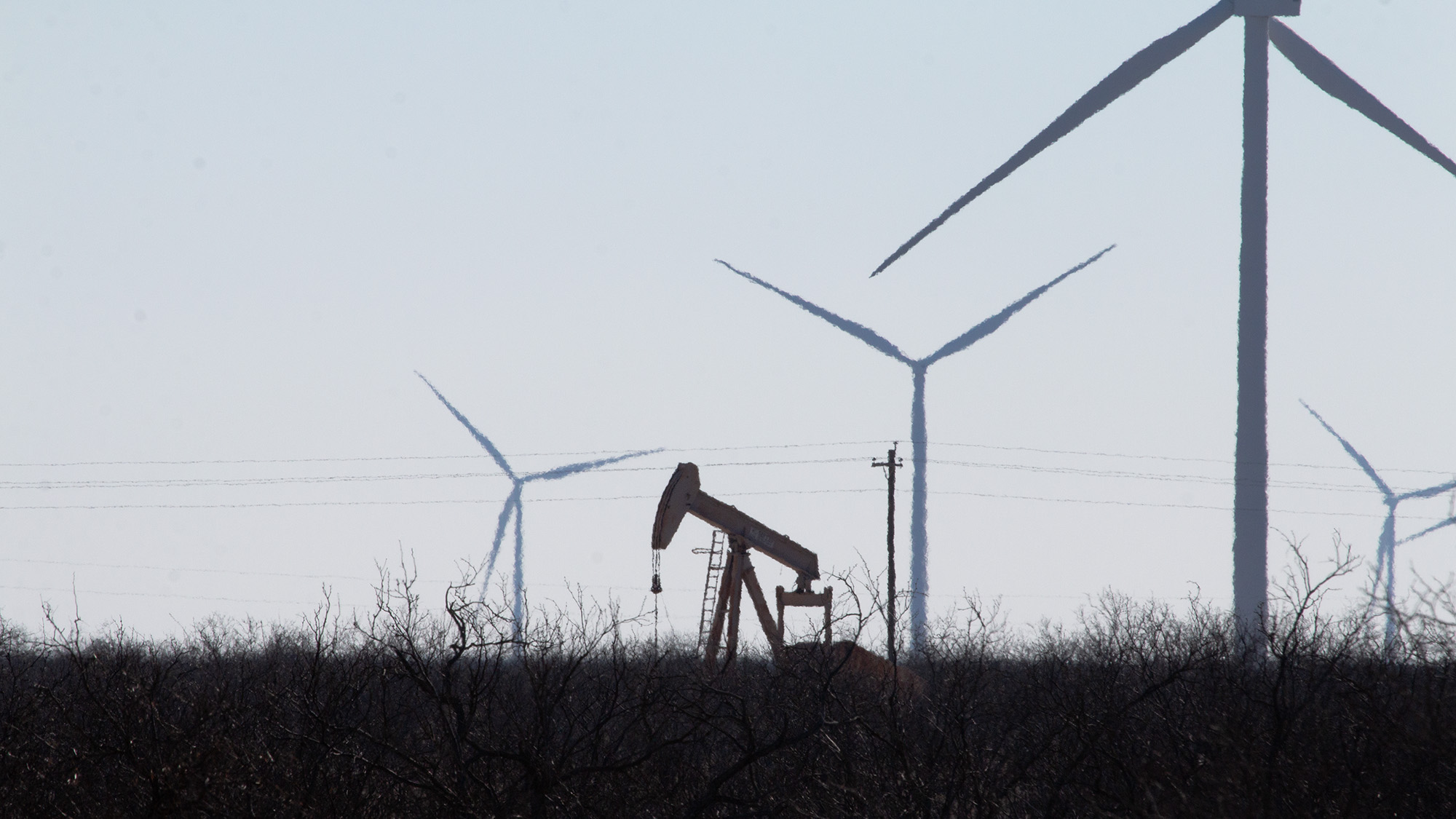 An oil pumpjack is seen in the same field as several wind turbines