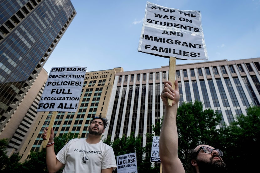 Demonstrators hold signs against the backdrop of the Earle Cabell Federal Building (right)...