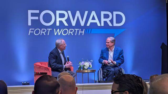 Two men on a stage sitting and talking with the words “Forward Fort Worth” behind them.