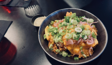 A close up of a bowl of chicken nuggets topped with cheese and green onions.
