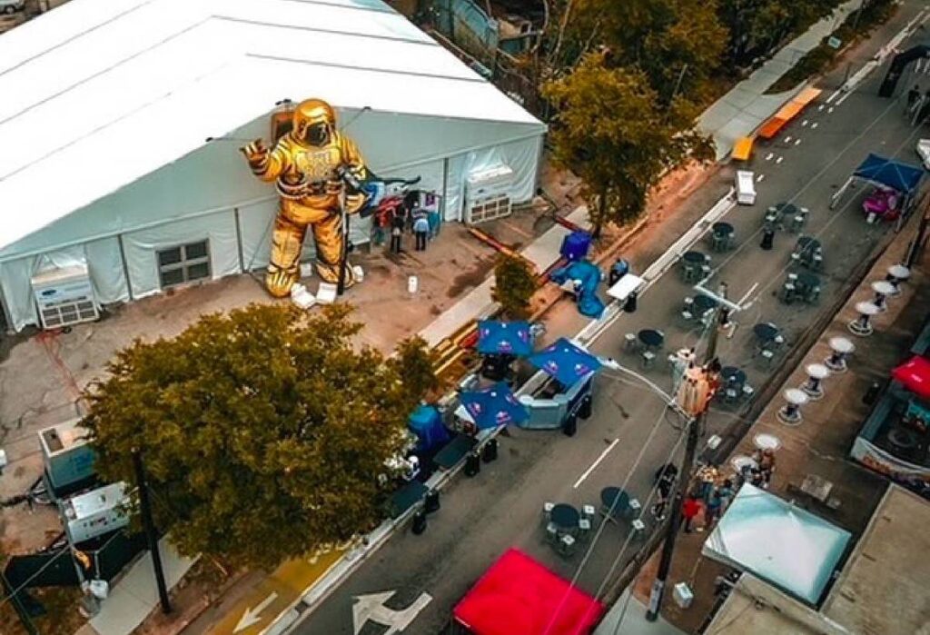 Bird's eye shot of the block party at The Riot Comedy Festival where a giant statue of an astronaut stands outside of a performance stage off the street.