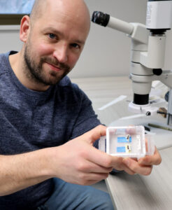 Silas Bossert holding a container with specimens of a new bee species near a microscope.