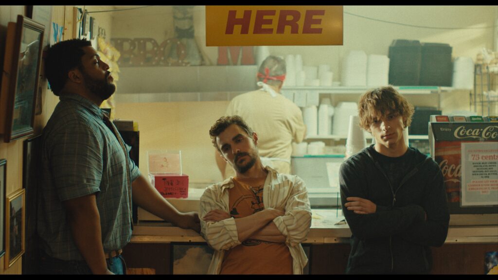 Actors O'Shea Jackson, Jr., Dave Franco and Mason Thames lean against what looks like a diner counter in the film "The Shitheads."