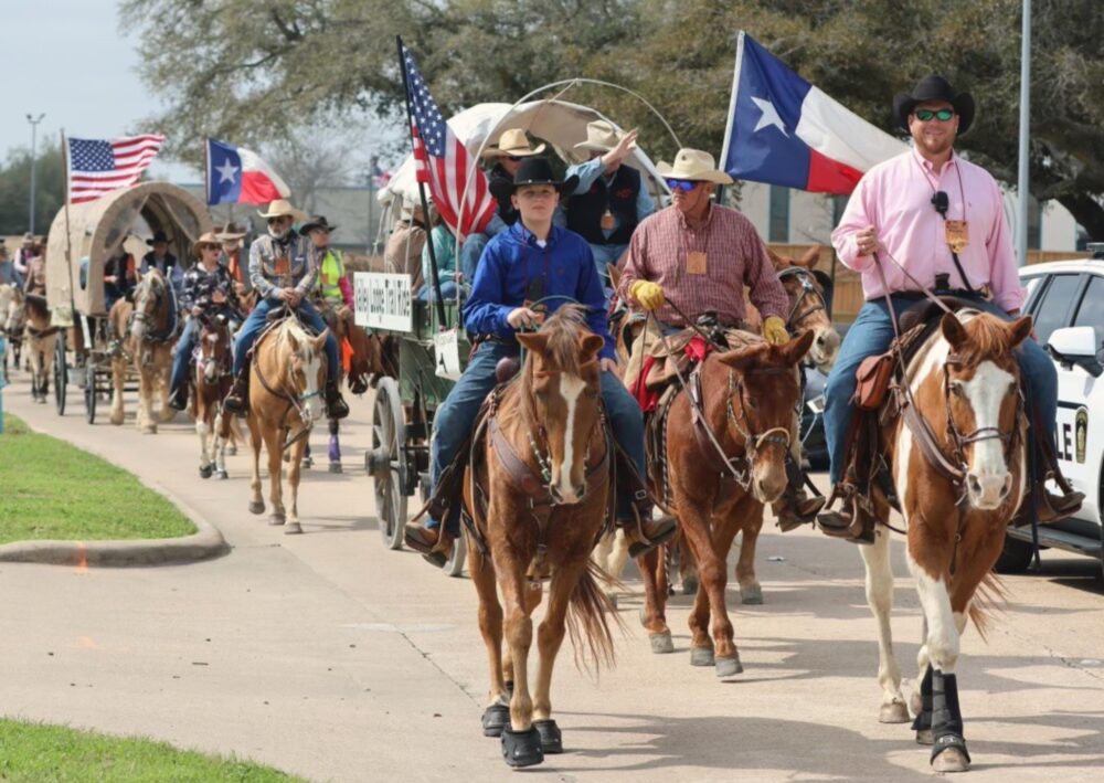 People on horses carrying flags ahead of covered wagons