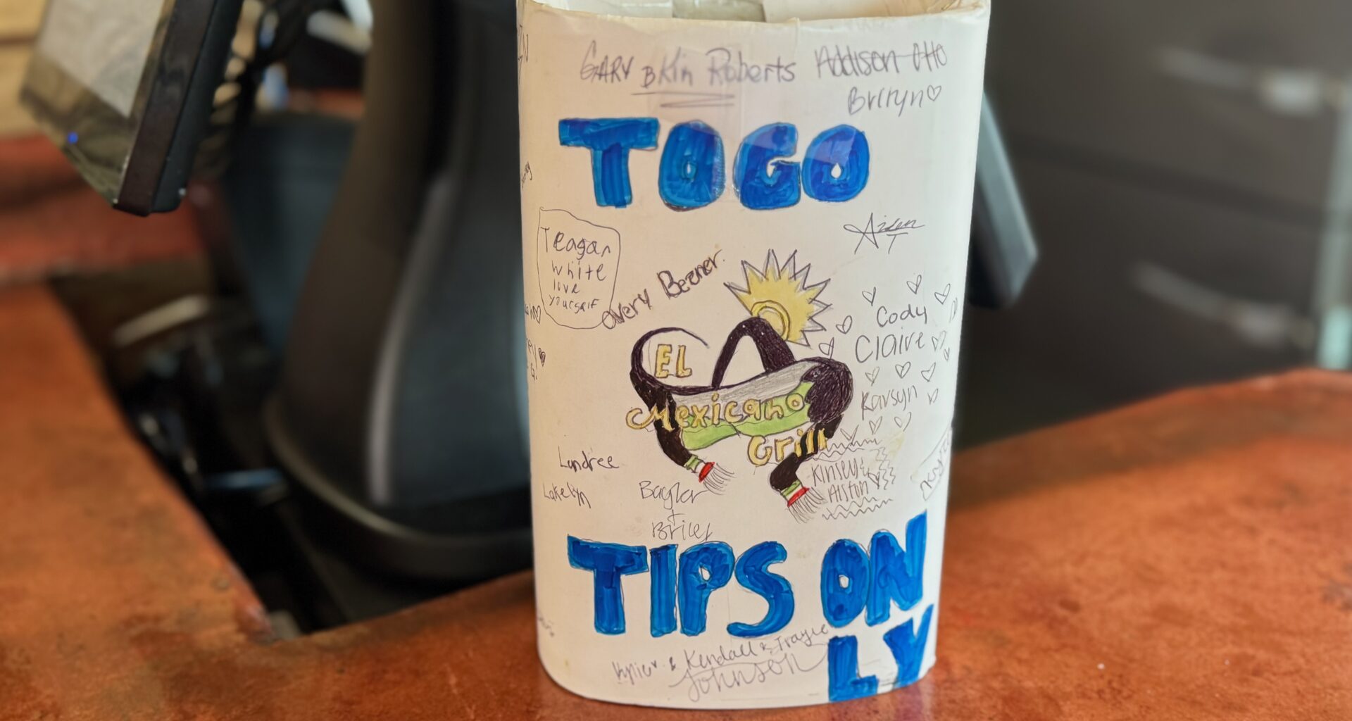 A brightly colored to-go tip jar on a counter of a restaurant.