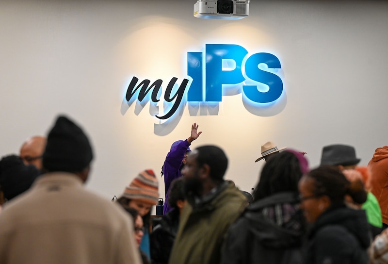 A group of people stand in a large room with an illuminated sign that reads "My IPS."