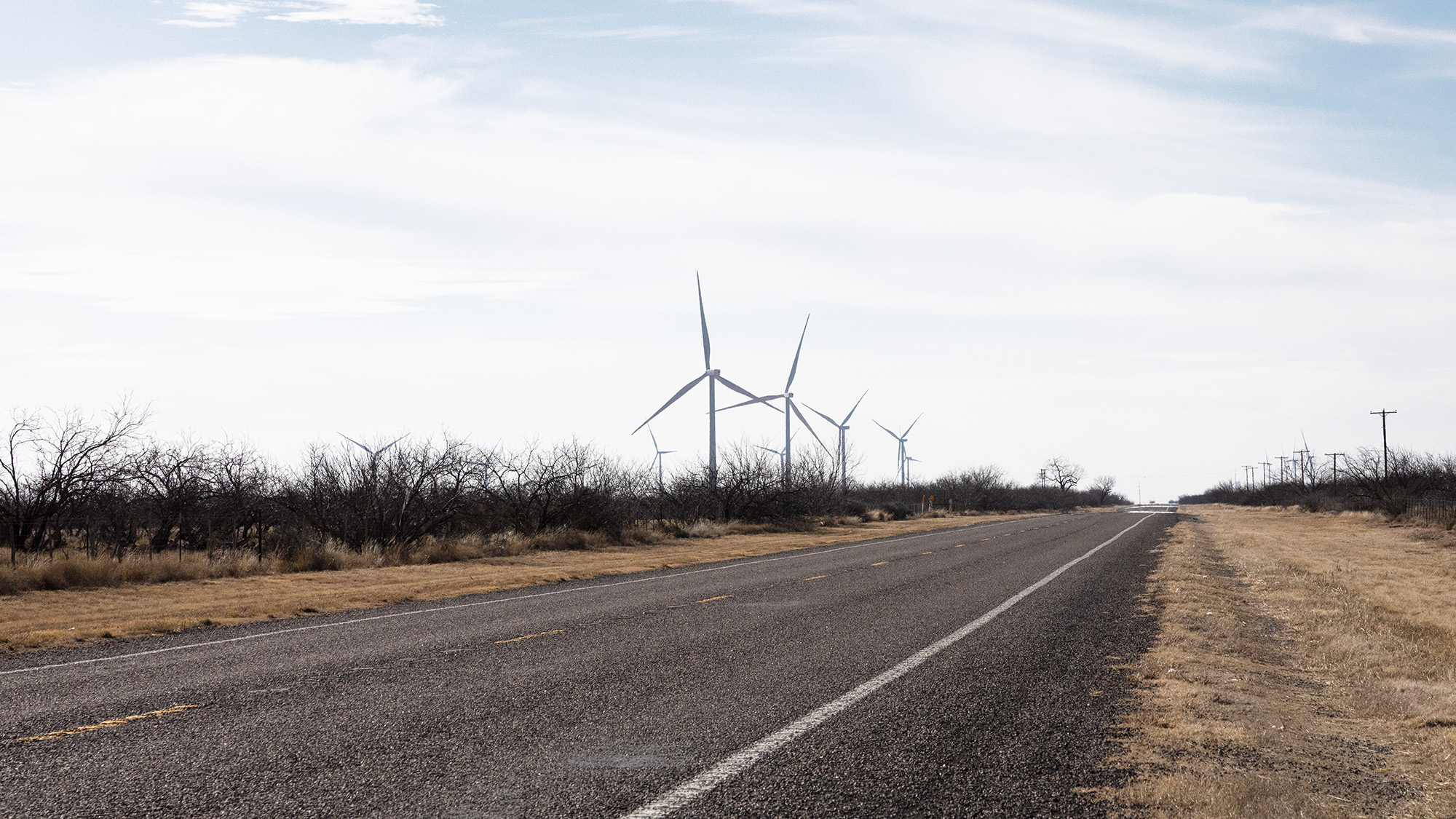 A stretch of open road runs past fields of wind turbines